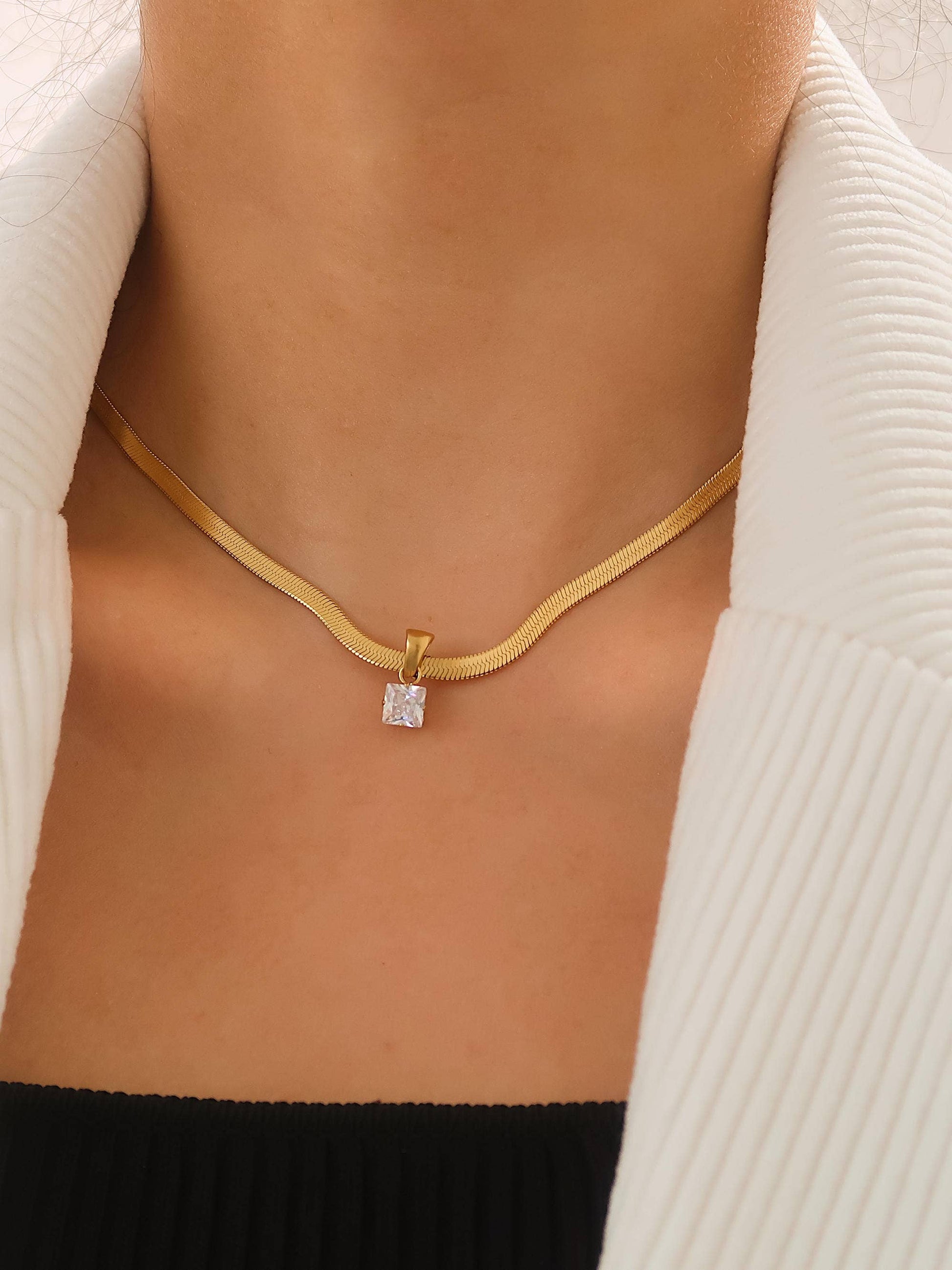Dainty 18K gold snake chain necklace with round CZ pendant, worn on woman's neckline
