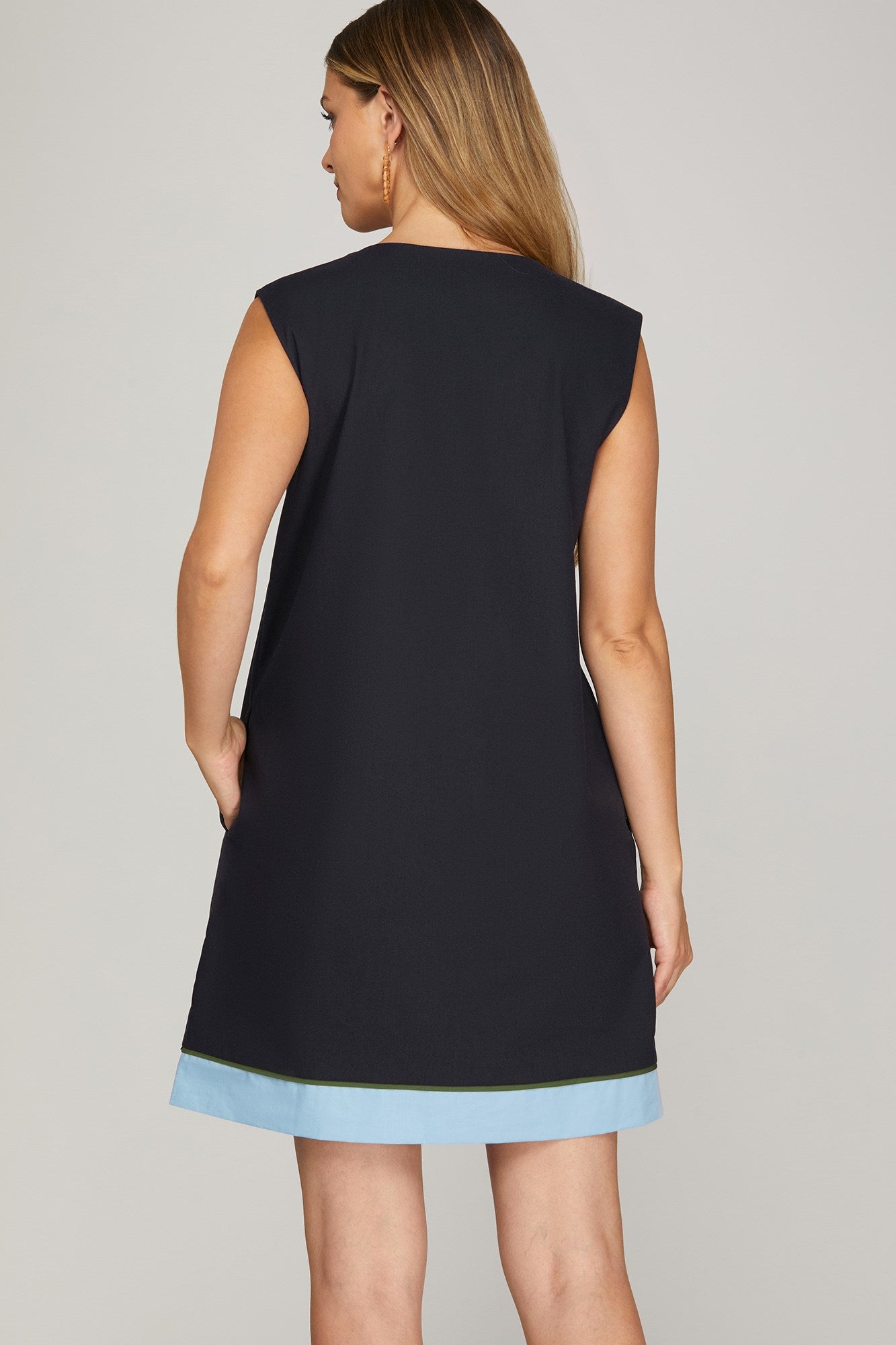 Woman wearing navy sleeveless mini shift dress with blue and white floral embroidery down the front, contrast sky-blue hem, and side pockets

