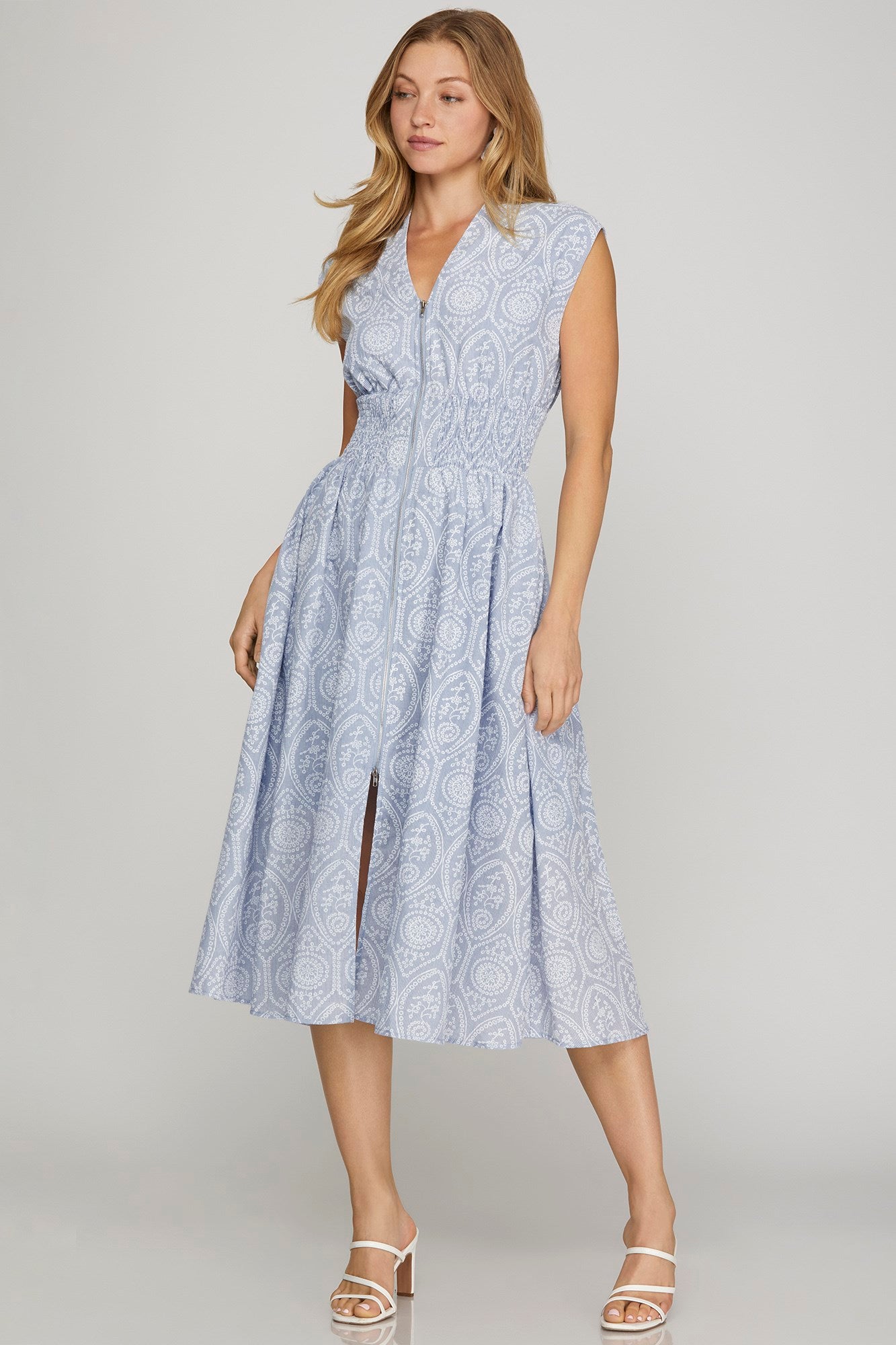 Woman wearing a sleeveless, light blue patterned dress on a plain background
