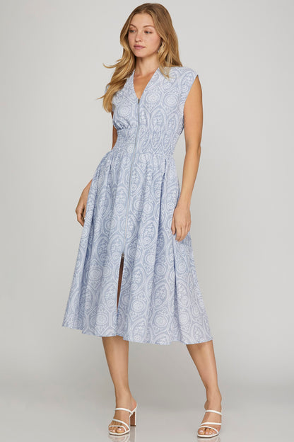 Woman wearing a sleeveless, light blue patterned dress on a plain background