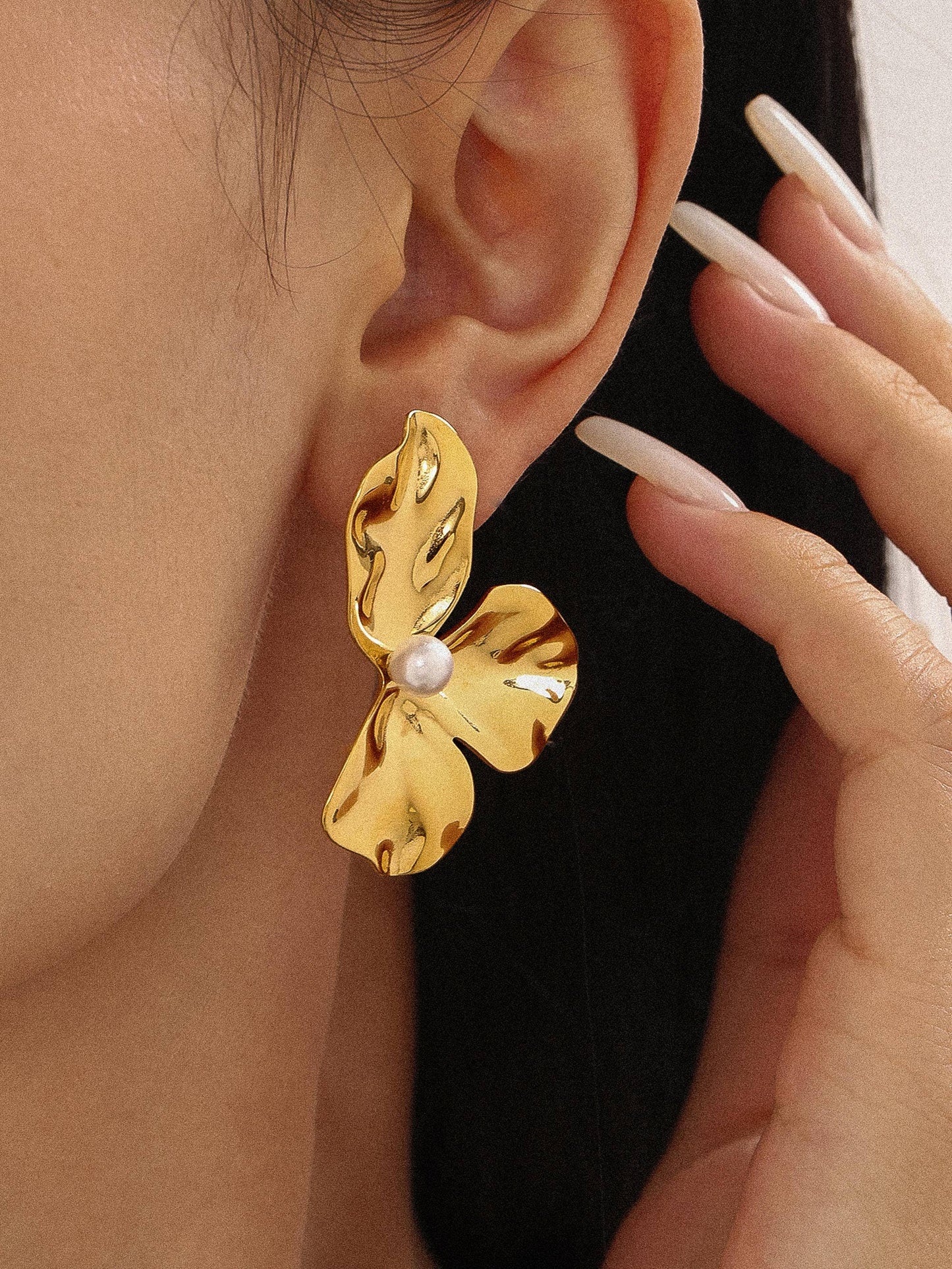 Woman wearing gold flower pearl drop earrings with casual outfit, statement jewelry close-up
